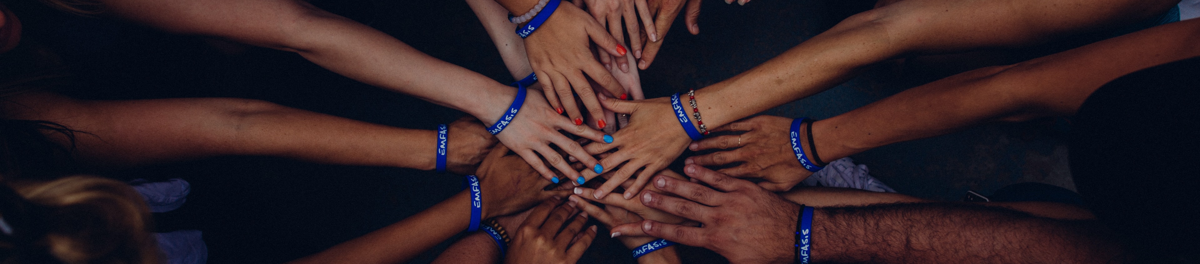 About Us. The featured image shows people putting their hands together in unity.